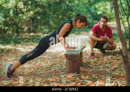 Woman doing push-ups in the park with personal trainer. Stock Photo