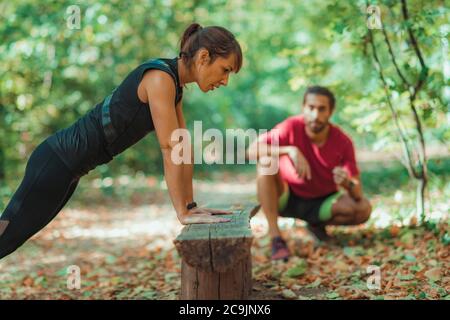 Woman doing push-ups in the park with personal trainer. Stock Photo