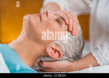 Marma therapy. Senior woman lying on massage table and enjoying Ayurveda facial treatment. Stock Photo