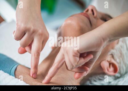 Marma therapy. Senior woman lying on massage table and enjoying Ayurveda neck treatment. Kanth Marma. Stock Photo