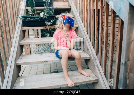 Adorable cute happy Caucasian girl holding Australian flag. Funny child kid covering her face with Australia flag. Little citizen celebrating Stock Photo