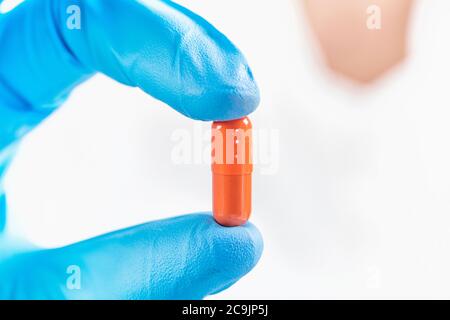 Scientist hand in glove holding orange pill with blue glove in laboratory. Stock Photo