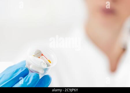 Female doctor's hand In blue glove holding graduated medicine cups full of pills. Copy space and white background. Stock Photo