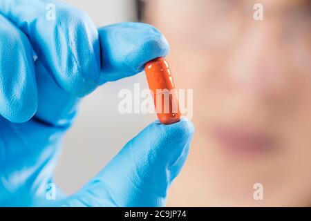 Scientist hand in glove holding orange pill with blue glove in laboratory. Stock Photo