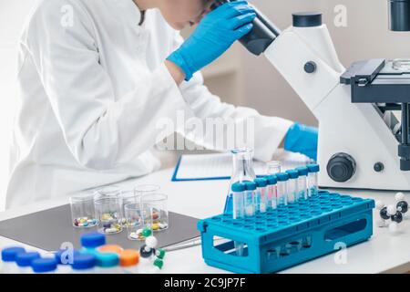 Medical researcher examining a new medicine. Female science student dressed in white lab coat looking through a microscope. Stock Photo