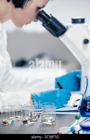 Medical researcher examining a new medicine. Female science student dressed in white lab coat looking through a microscope. Stock Photo