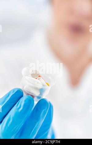 Female doctor's hand In blue glove holding graduated medicine cups full of pills. Copy space and white background. Stock Photo