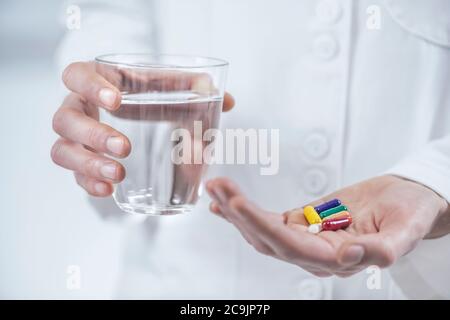 Doctor's hand holding colourful pills and glass of water. Stock Photo