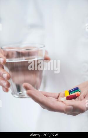 Doctor's hand holding colourful pills and glass of water. Stock Photo