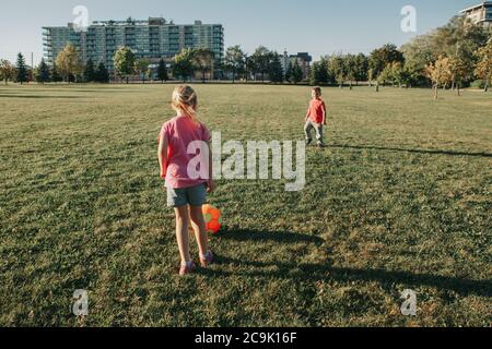 Little preschool girl and boy friends playing soccer football on playground grass field outside. Happy authentic candid childhood lifestyle.