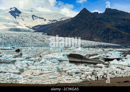 Group of tourists are standing and looking at the amazing views of the Fjallsarlon mountains and lakes with large glaciers and icebergs floating in th Stock Photo