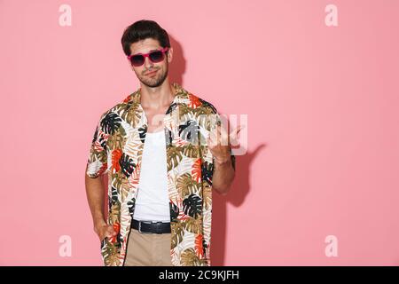 Portrait of displeased young man in sunglasses pointing fingers aside isolated over pink background Stock Photo