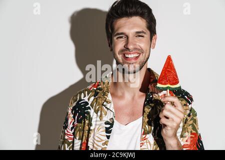Portrait of cheerful man in flamboyant shirt laughing while posing with lollipop isolated over white background Stock Photo