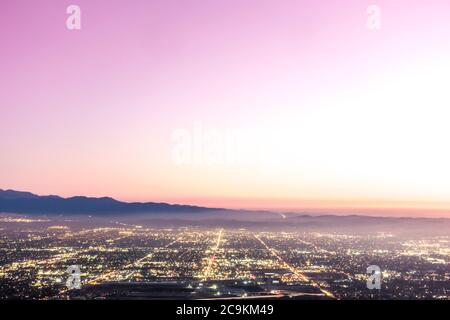 The city lights of the skyline of the Inland Empire near Los Angeles California begin to appear as the sun sets in a dramatic pink sunset. Stock Photo