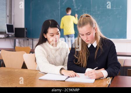 Tired female students during writing notes in classroom,  male student writing on whiteboard Stock Photo