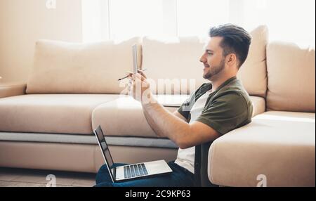 Bearded caucasian man working on the floor with a tablet and laptop having a video meeting Stock Photo