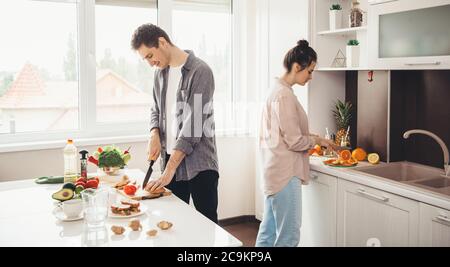 Young caucasian couple slicing fruits in the kitchen and preparing breakfast together Stock Photo