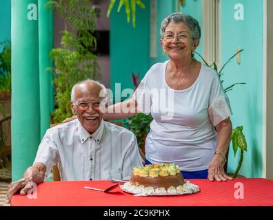 Smiling elderly couple sitting in front of a cake Stock Photo