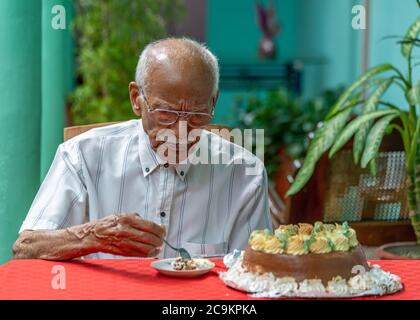 Elderly man sitting at a table eating cake Stock Photo