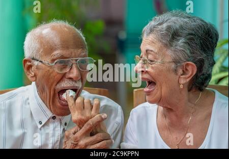 Elderly couple looking at each other smilingly. The old woman giving meringue cake to the old man Stock Photo
