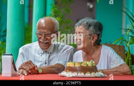 Smiling elderly couple sitting at a table looking at a cell phone Stock Photo
