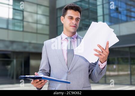 Businessman holding folder with documents and attentively reading Stock Photo