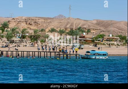 People stand on a jetty watching people swim in the Gulf of Aqaba. Aqaba has excellent diving and snorkeling reefs. Stock Photo