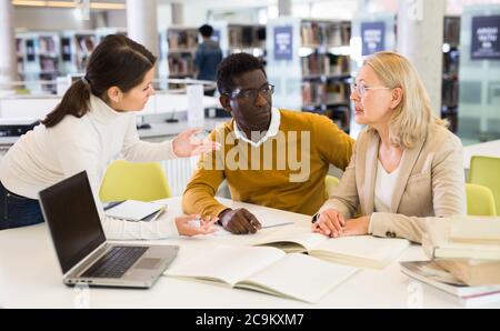 Female tutor helping students preparing for exam in library Stock Photo