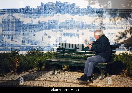 LISBON, PORTUGAL - FEBRUARY 2, 2019: Old man reading a newspaper sitting on a bench next to azulejos decorated wall of the church of Santa Luzia, land Stock Photo