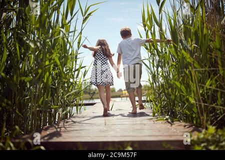 Brother and sister barefoot walking on the dock of the lake Stock Photo