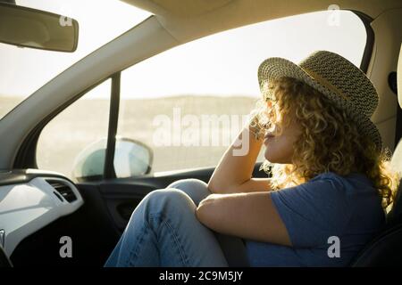 one, beautiful curly woman enjoying her vacations outdoors traveling with a car - sunset and sunny day at the background - relaxed and serene person Stock Photo