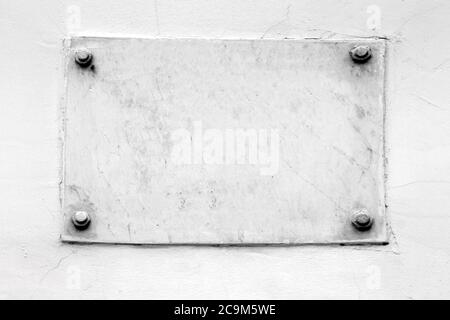 Board in the form of a piece of marble is attached to a white wall with four bolts. Place for text Stock Photo