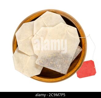 Tea bags in wooden bowl. Small, porous, sealed bag, made of filter paper, with attached string, containing shredded tea, to make an infusion. Stock Photo