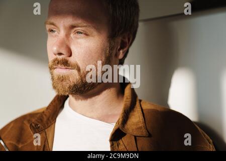 Photo closeup of thinking young man with ginger beard posing and looking aside indoors Stock Photo