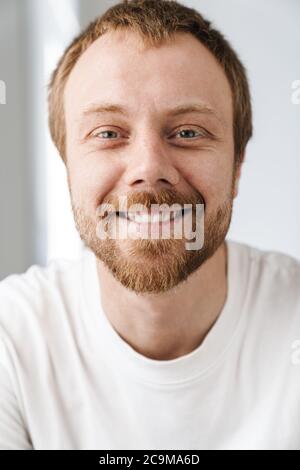 Photo of joyful handsome man with red hair posing and smiling on camera indoors Stock Photo