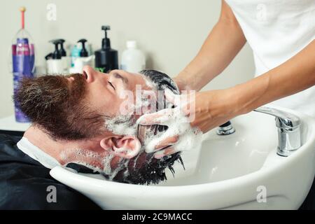 Close-up of brutal caucasian man having his hair washed in hairdressing salon. Barber washing head client. Barber at work. Stock Photo