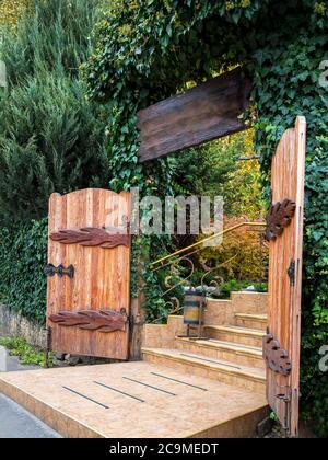 The entrance to the wooden gate is overgrown with ivy and other evergreens, the passage to the territory of the house is tiled in front of the steps. Stock Photo