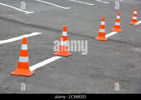 Road cones orange color enclose freshly painted markings on old asphalt with cracks, close up nobody. Stock Photo