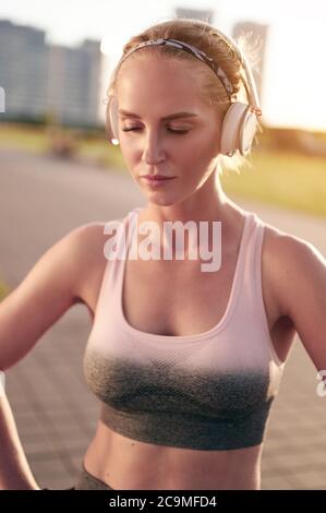 Exhausted sporty fit woman in fitness clothing relaxing while doing physical exercise and listening to music in headphones Stock Photo