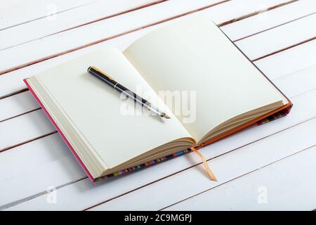 the ink handle lies on empty pages of a notebook with blank sheets which lies on white wooden board, a fountain pen from a notebook on a table. Stock Photo