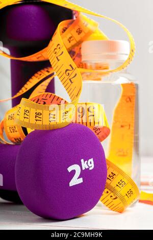 dumbbells weight for fitness violet color with yellow tape measure on white wooden board and water bottle. Stock Photo