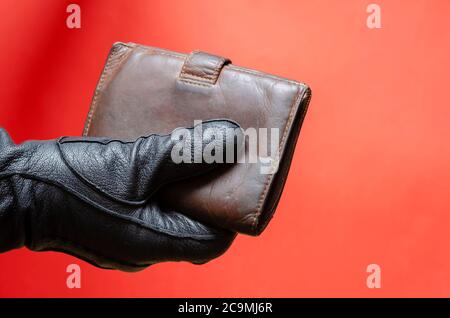 Hand in black leather glove holds out brown wallet. Male hand holds wallet to pay for purchase or theft concept. Side view. Selective focus. Stock Photo