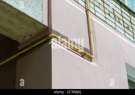 Yellow gas pipe viewed on the outer brick wall of residential building. Facade of multi-storey apartments with gas pipeline. Partial thermal insulatio Stock Photo