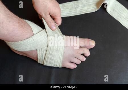 Middle-aged Caucasian man produces an independent bandage of his dislocated leg. He puts an elastic bandage over his swollen shin. First aid in sprain Stock Photo