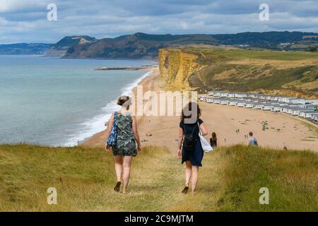 Burton Bradstock, Dorset, UK.  1st August 2020.  UK Weather. Walkers on the South West Coast Path take in the spectacular views from the cliff top path as they walk from Burton Bradstock to West Bay in Dorset on a day of hot sunny spells.  Ahead of them is Freshwater Beach Holiday Park and the famous sandstone cliffs at West Bay.  Picture Credit: Graham Hunt/Alamy Live News Stock Photo