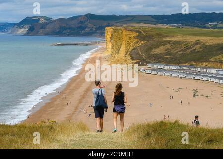 Burton Bradstock, Dorset, UK.  1st August 2020.  UK Weather. Walkers on the South West Coast Path take in the spectacular views from the cliff top path as they walk from Burton Bradstock to West Bay in Dorset on a day of hot sunny spells.  Ahead of them is Freshwater Beach Holiday Park and the famous sandstone cliffs at West Bay.  Picture Credit: Graham Hunt/Alamy Live News Stock Photo