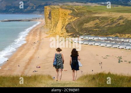 Burton Bradstock, Dorset, UK.  1st August 2020.  UK Weather. Walkers on the South West Coast Path take in the spectacular views from the cliff top path as they walk from Burton Bradstock to West Bay in Dorset on a day of hot sunny spells.  Ahead of them is Freshwater Beach Holiday Park and the famous sandstone cliffs at West Bay.  Picture Credit: Graham Hunt/Alamy Live News Stock Photo