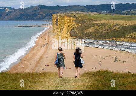 Burton Bradstock, Dorset, UK.  1st August 2020.  UK Weather. Walkers on the South West Coast Path take in the spectacular views from the cliff top path as they walk from Burton Bradstock to West Bay in Dorset on a day of hot sunny spells.  Ahead of them is Freshwater Beach Holiday Park and the famous sandstone cliffs at West Bay.  Picture Credit: Graham Hunt/Alamy Live News Stock Photo