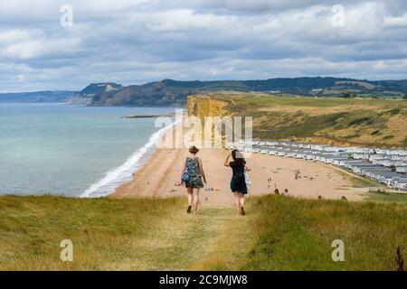 Burton Bradstock, Dorset, UK.  1st August 2020.  UK Weather. Walkers on the South West Coast Path take in the spectacular views from the cliff top path as they walk from Burton Bradstock to West Bay in Dorset on a day of hot sunny spells.  Ahead of them is Freshwater Beach Holiday Park and the famous sandstone cliffs at West Bay.  Picture Credit: Graham Hunt/Alamy Live News Stock Photo