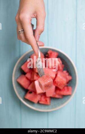 watermelon in a plate on a blue background and a hand holds a fork with a slice of watermelon Stock Photo